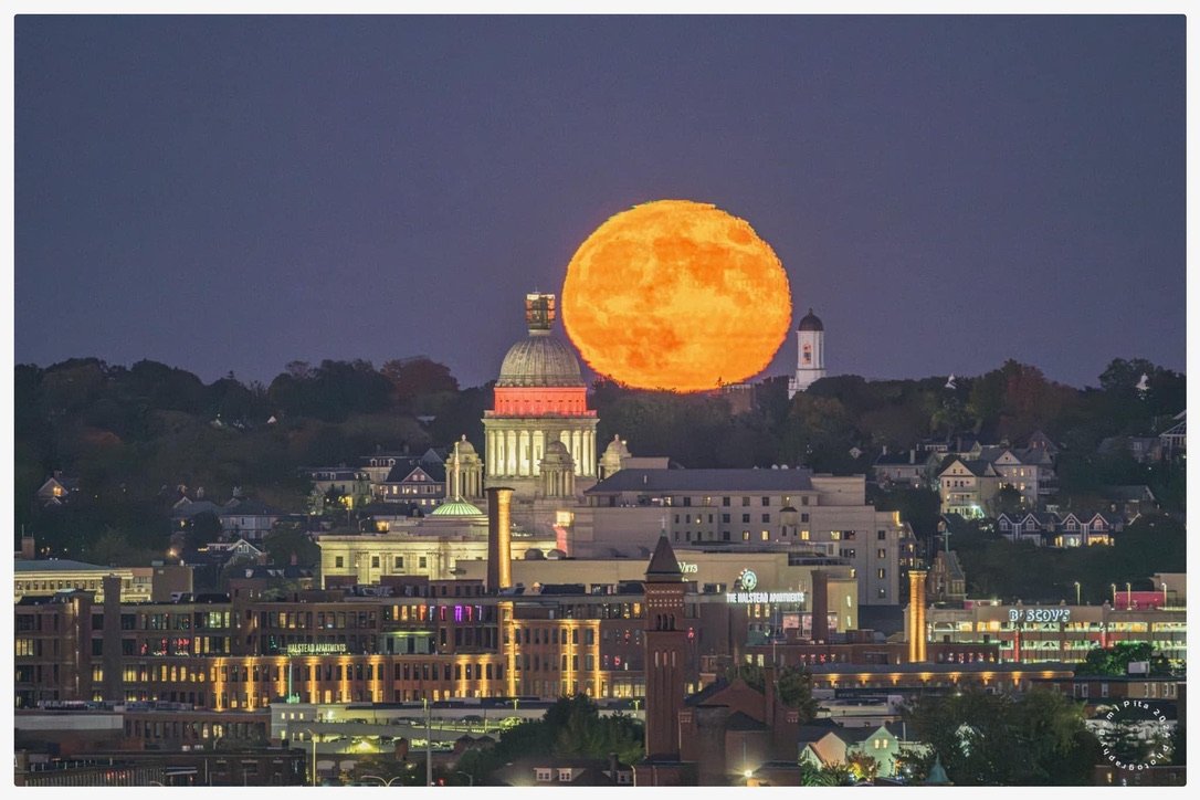 Supermoon rising over cityscape with prominent dome building, twilight setting.
