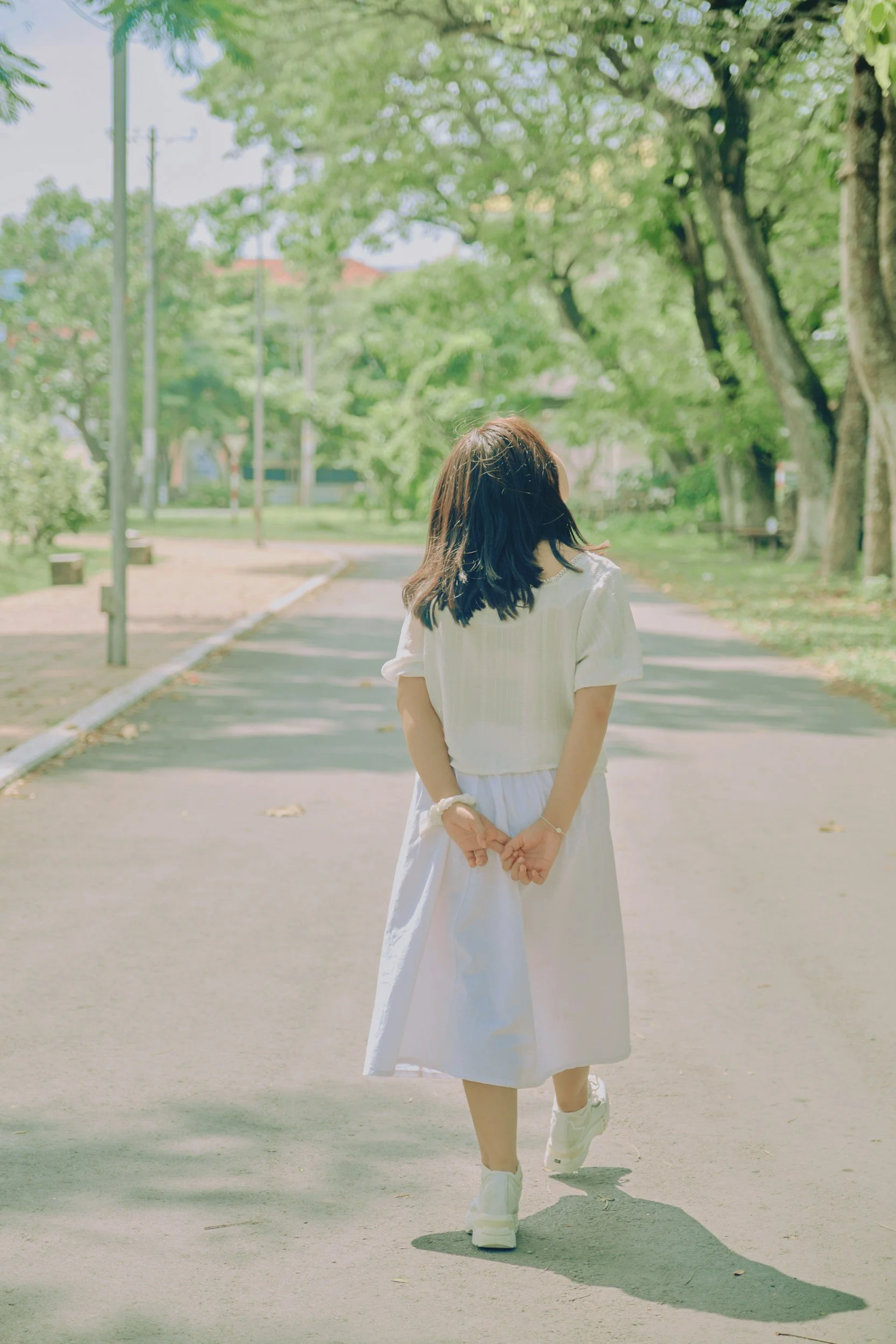 Young girl in a dress walking along a tree filled street