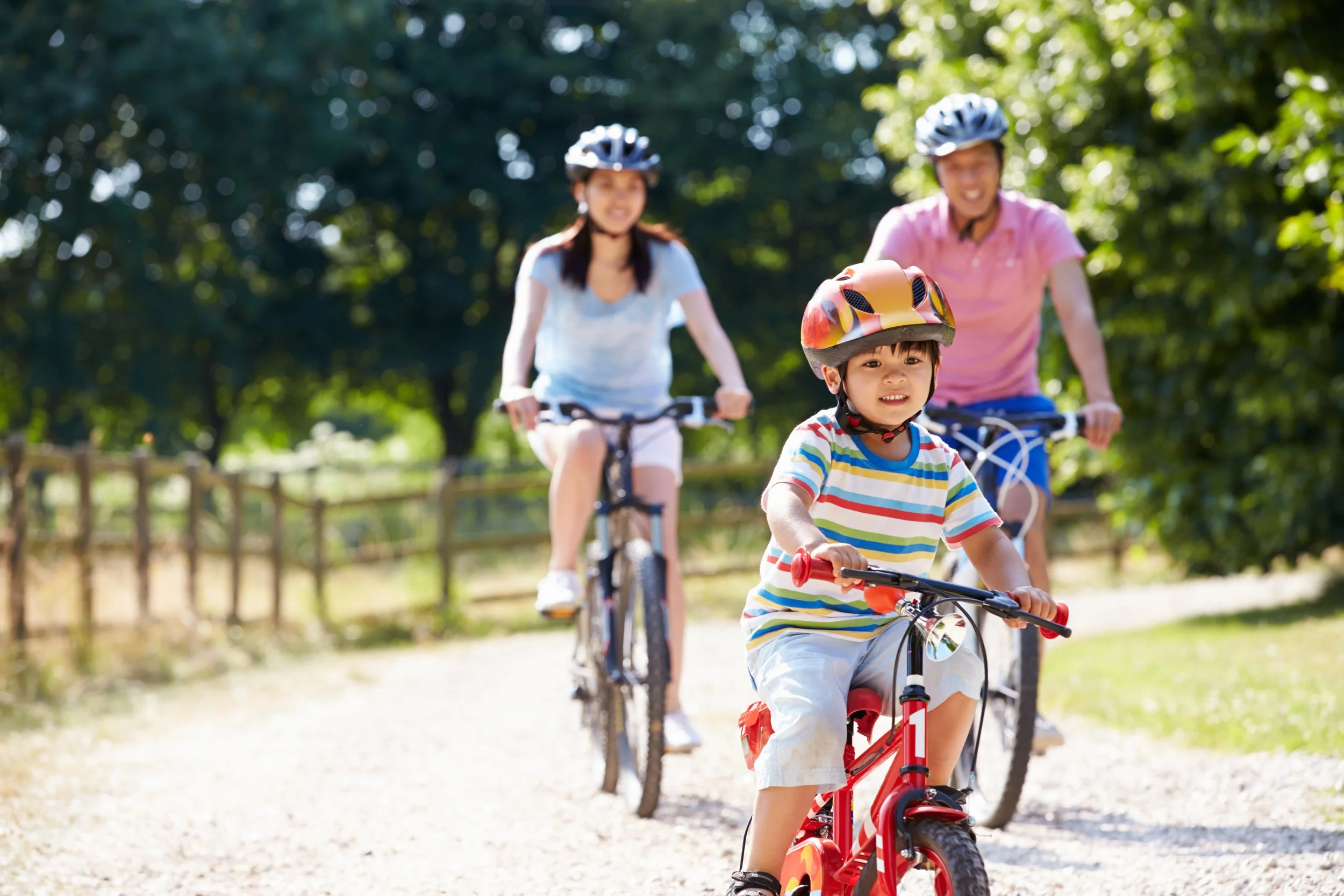 Child riding on his bike with his helmet on, parents riding behind him.