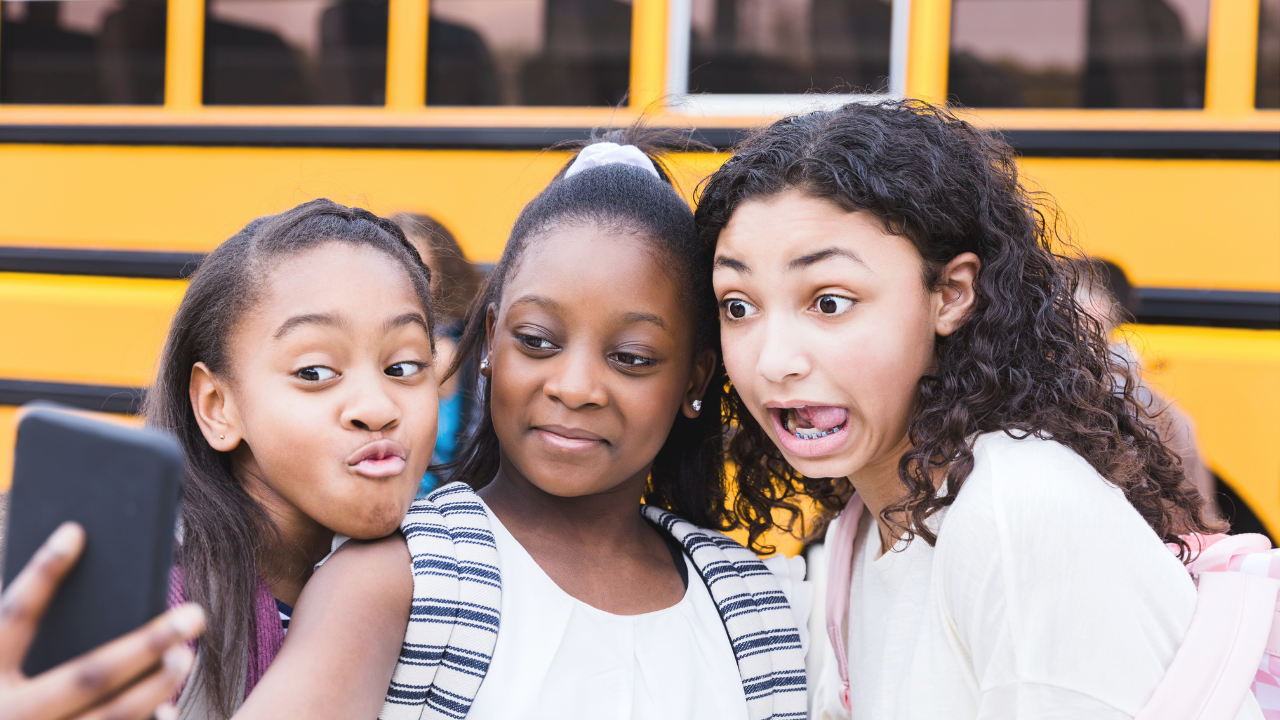 Three tween girls taking a selfie in front of a school bus