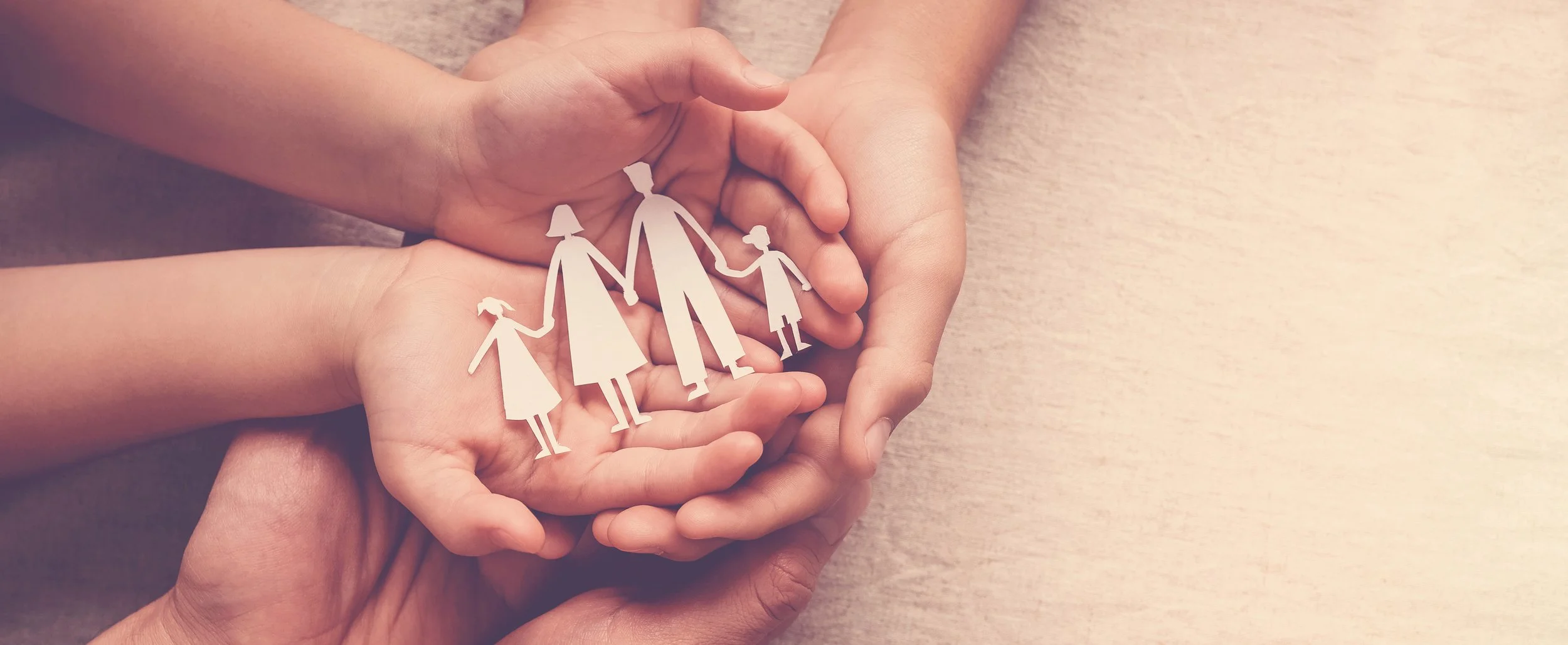 "A family holding hands, with a paper cut-out of a family in the center, symbolizing support, care, and unity."