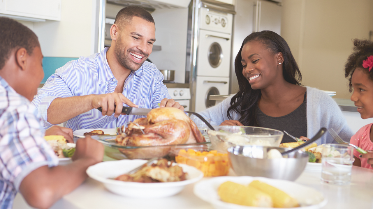 Mom, Dad, and two children enjoying a meal at the table while Dad is cutting the turkey.