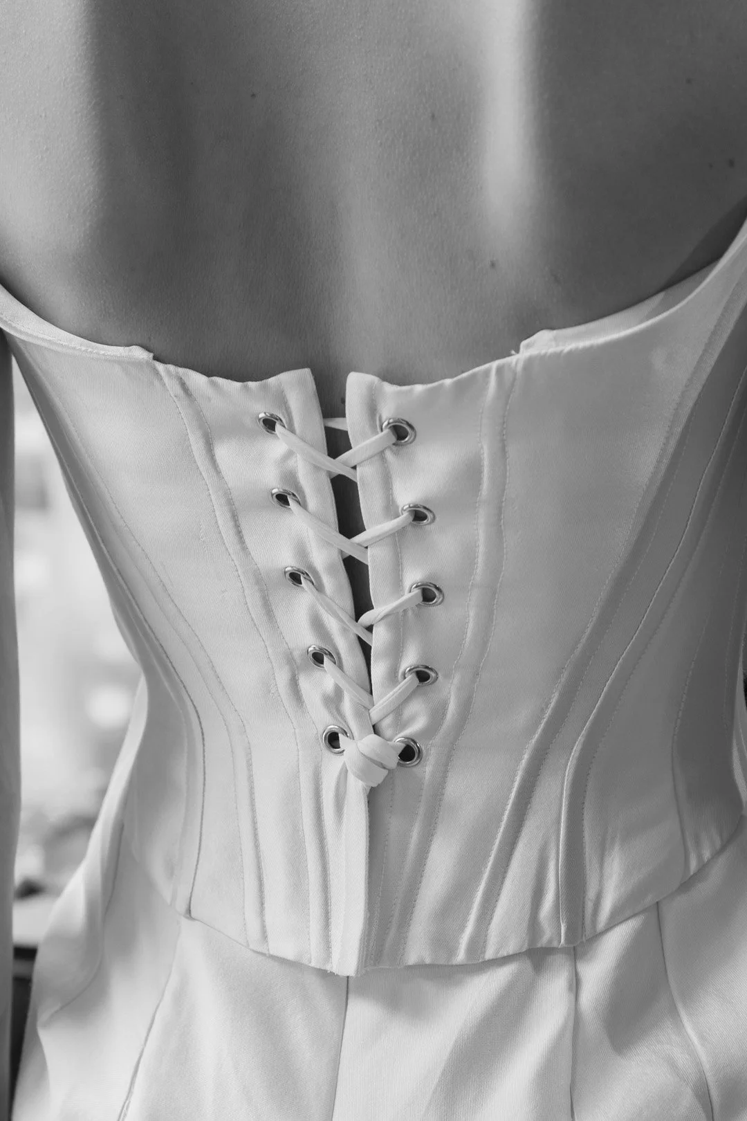 Close-up of a satin corset with lace-up front on a mannequin in black and white.