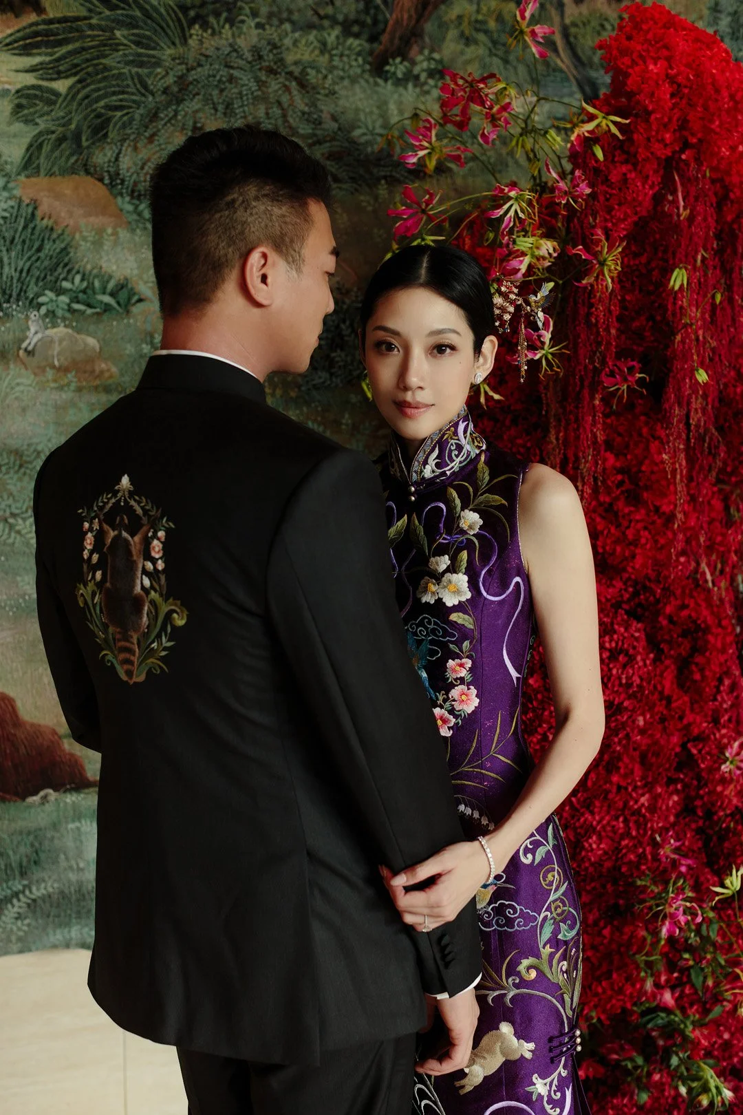 A man and woman dressed in formal attire standing close together against a floral backdrop.