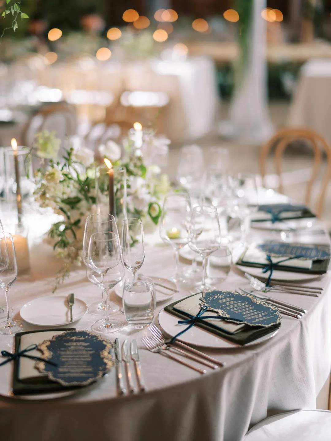 Elegant dining table set with wine glasses, floral centerpiece, candles, and menus, in a softly lit venue