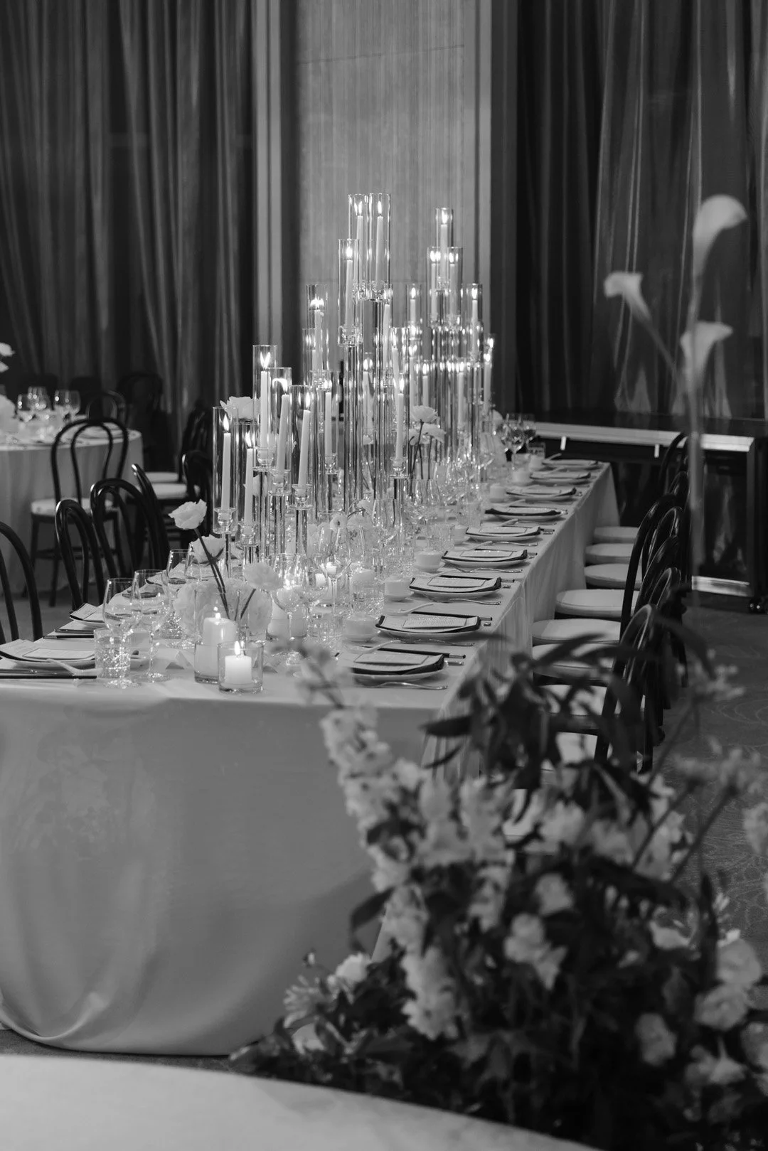 Elegant dining table decorated with tall candles, flowers, and tableware in a formal event setting.