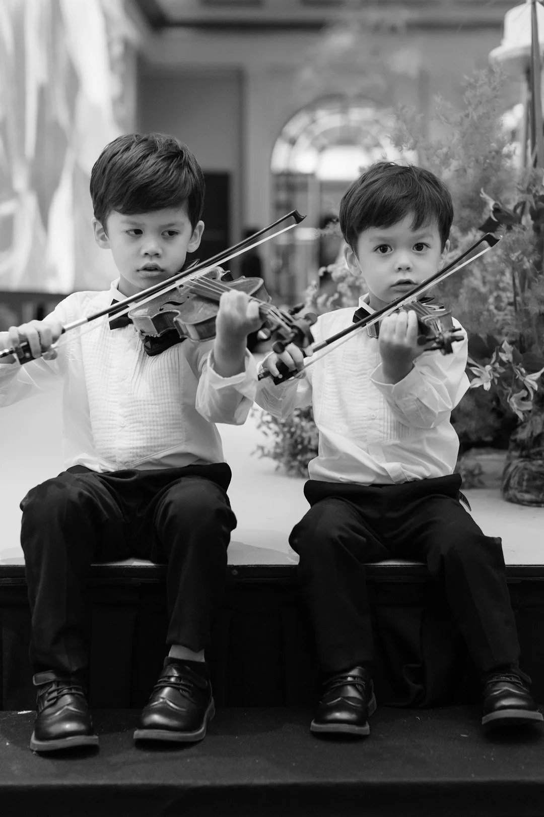 Two young boys in formal attire playing violins together on stage.