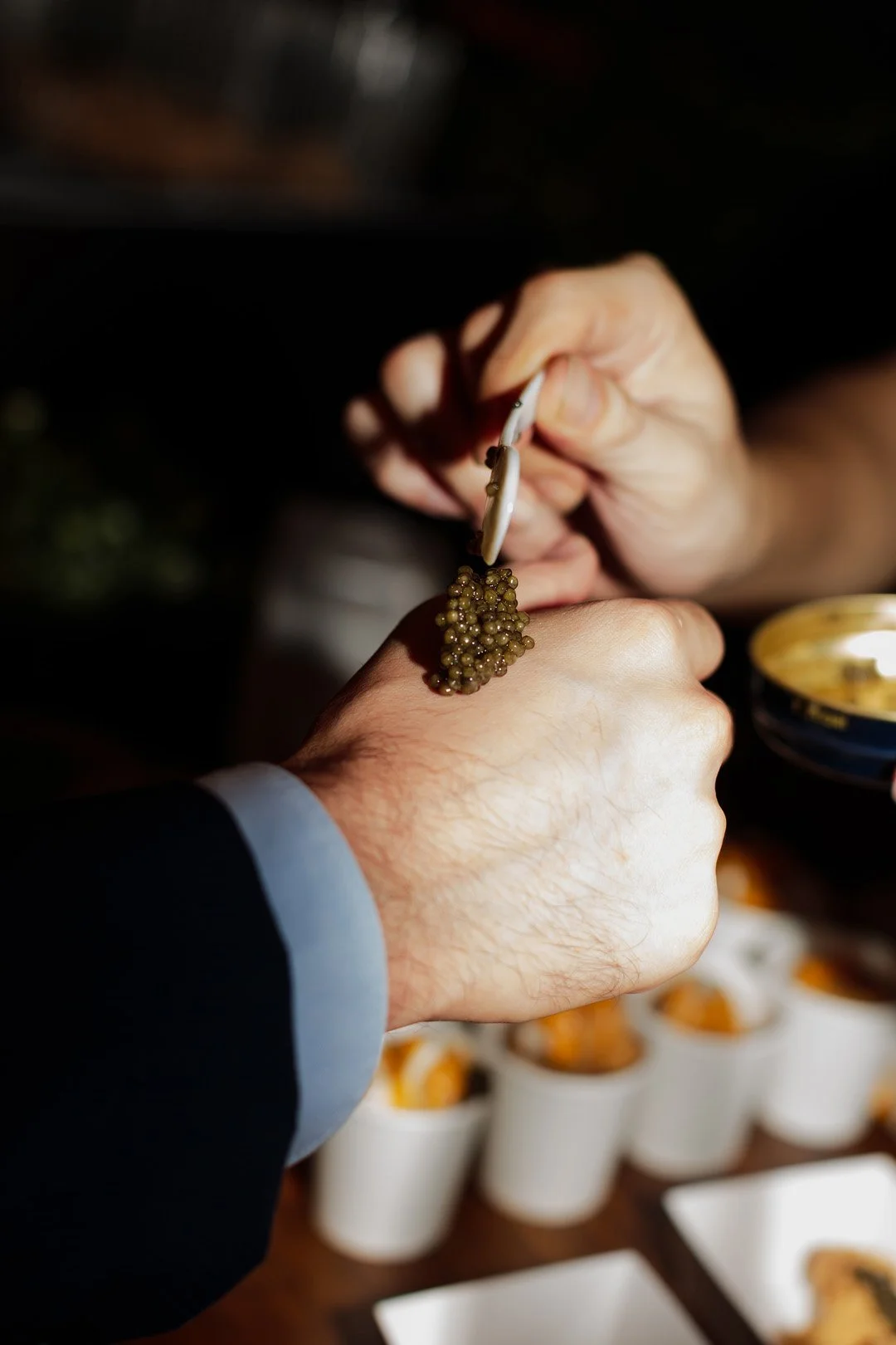 Person using tweezers to handle caviar on their hand during a tasting or presentation.
