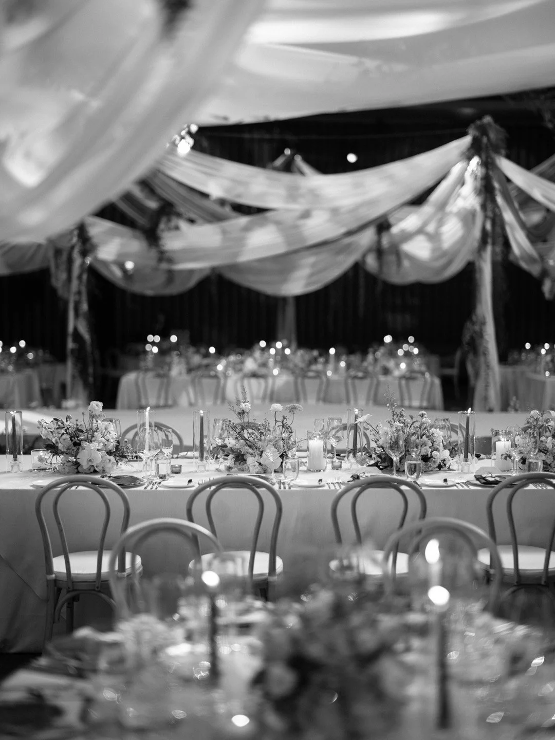 Elegant banquet hall with long tables decorated with floral centerpieces and candles, draped fabric ceiling, and chairs arranged for a formal event.
