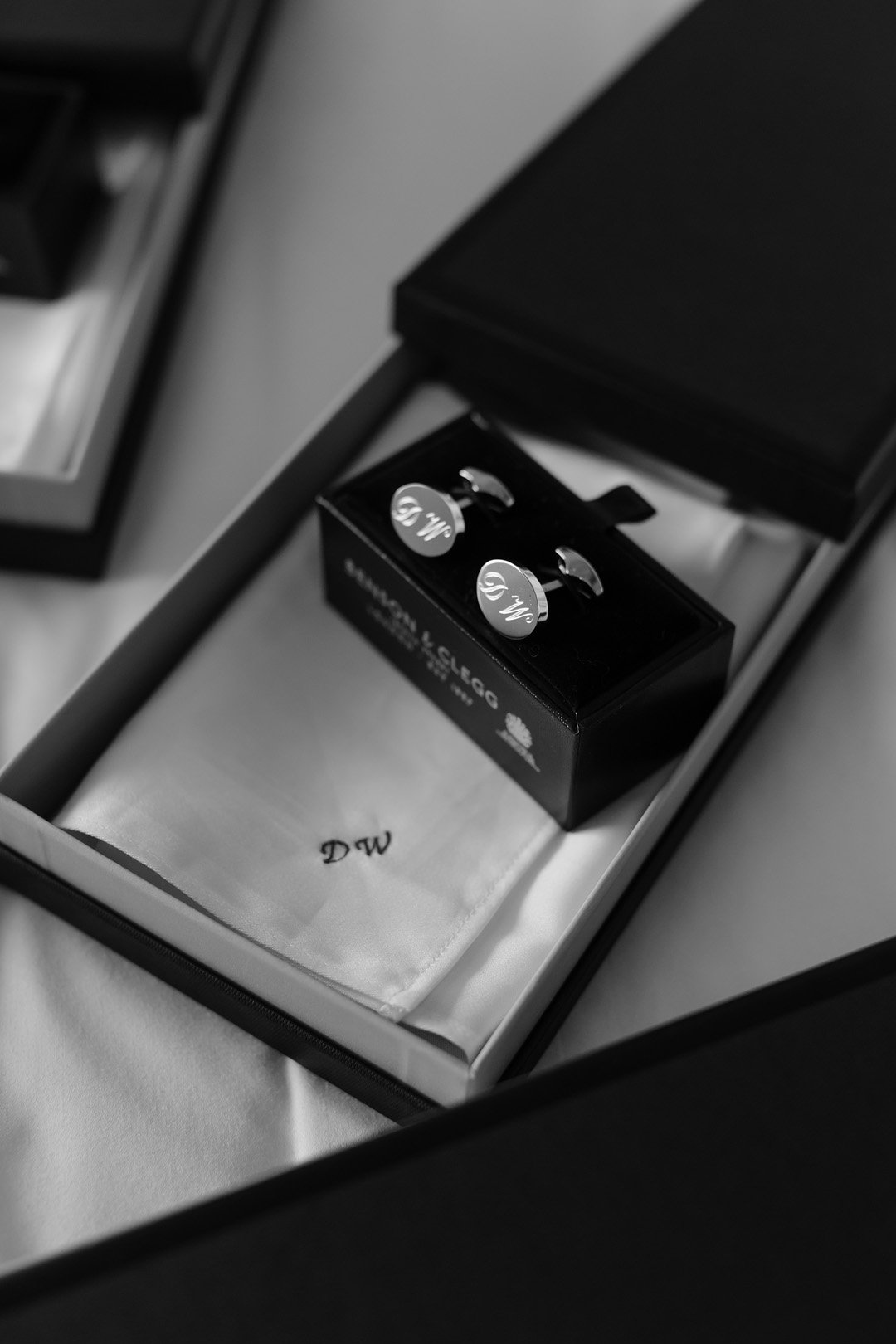 Black and white photo of a box containing a pair of cufflinks and a cloth with initials 'DW' embroidered on it.