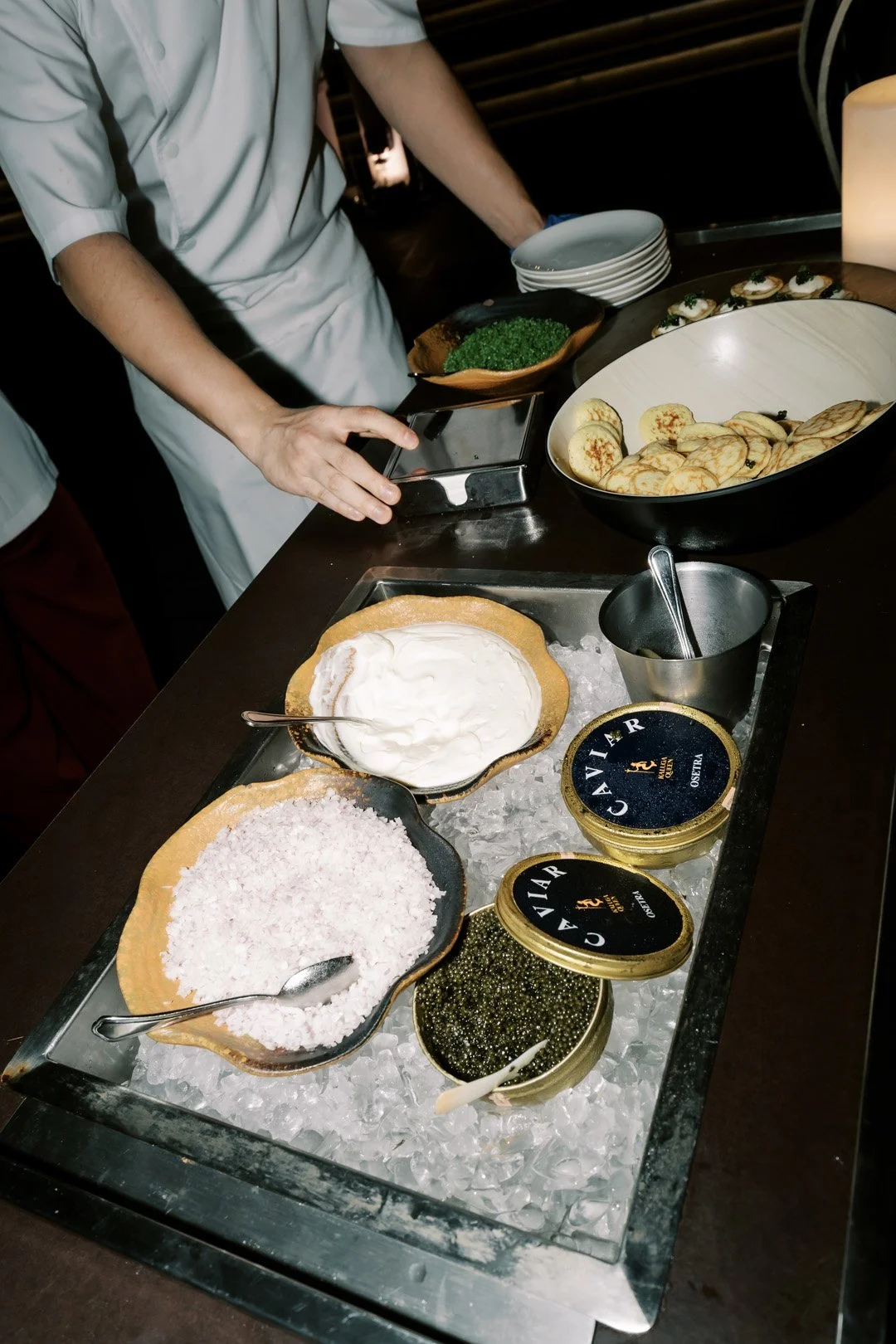 Display of caviar, cream cheese, and other gourmet toppings in bowls on a bed of ice at a buffet.
