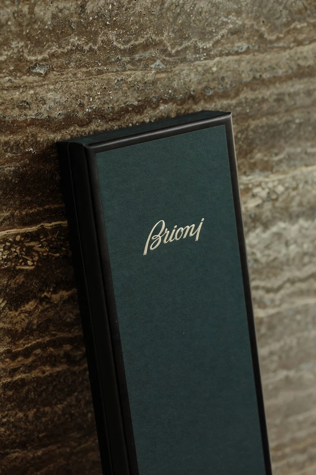 A menu with the word 'Brioni' written on it, leaning against a textured stone wall.