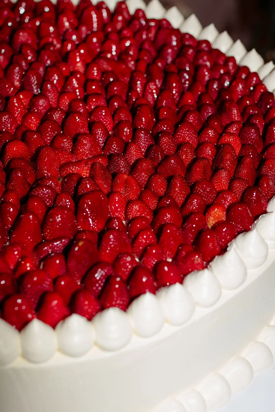 A cake decorated with a border of white icing dots and topped with a large number of fresh strawberries.