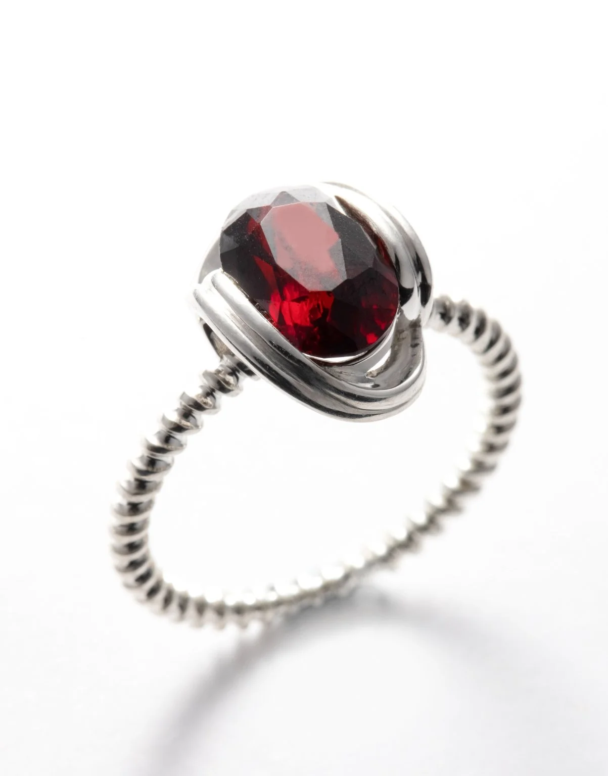 Silver ring with a red gemstone set in a bezel setting against a white background.