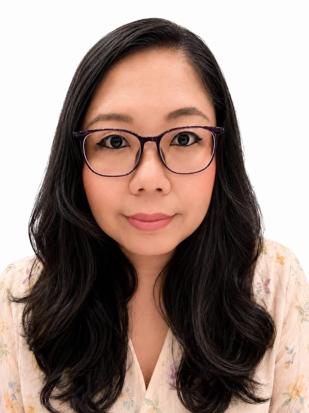 A woman with long dark hair, wearing glasses, and a light-colored floral top, looking directly at the camera with a neutral expression.