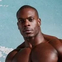A portrait of a muscular man with dark skin and short hair, posing shirtless against a plain background.