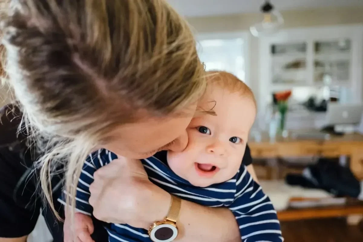 Mother holding and kissing a smiling baby at home