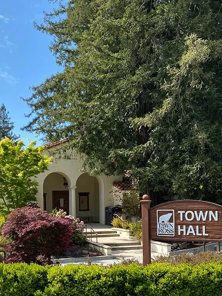 Town hall building with an arched entrance, surrounded by trees and bushes, and a sign that reads "Town Hall" in Ross.