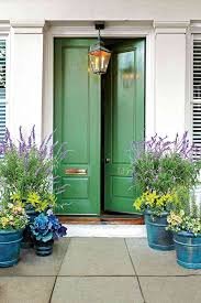 Green front door with a lantern hanging above, surrounded by potted purple and yellow flowers.