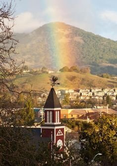 A rainbow over a mountain with a small church and trees in the foreground.