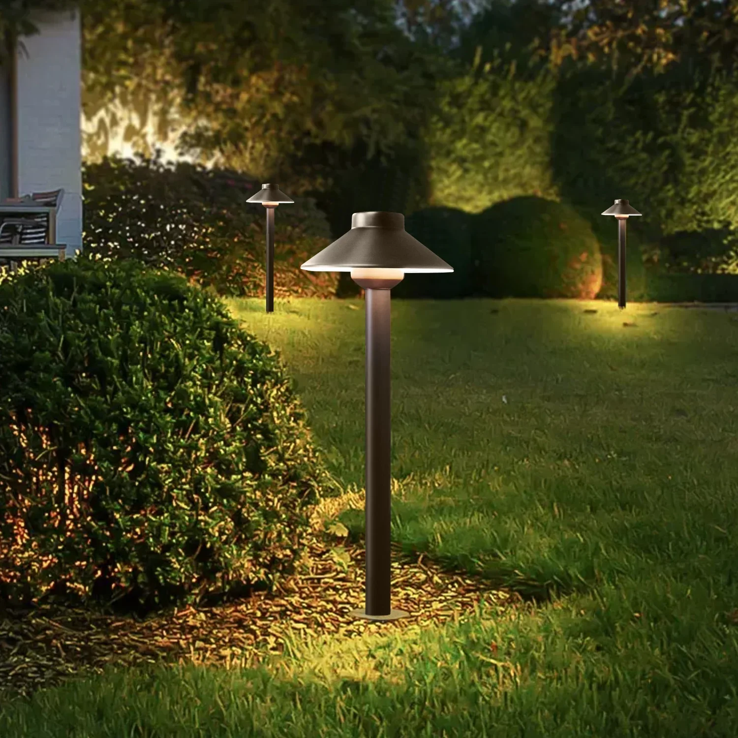 Outdoor garden pathway with three pathway lights illuminating the grass and hedge at night.