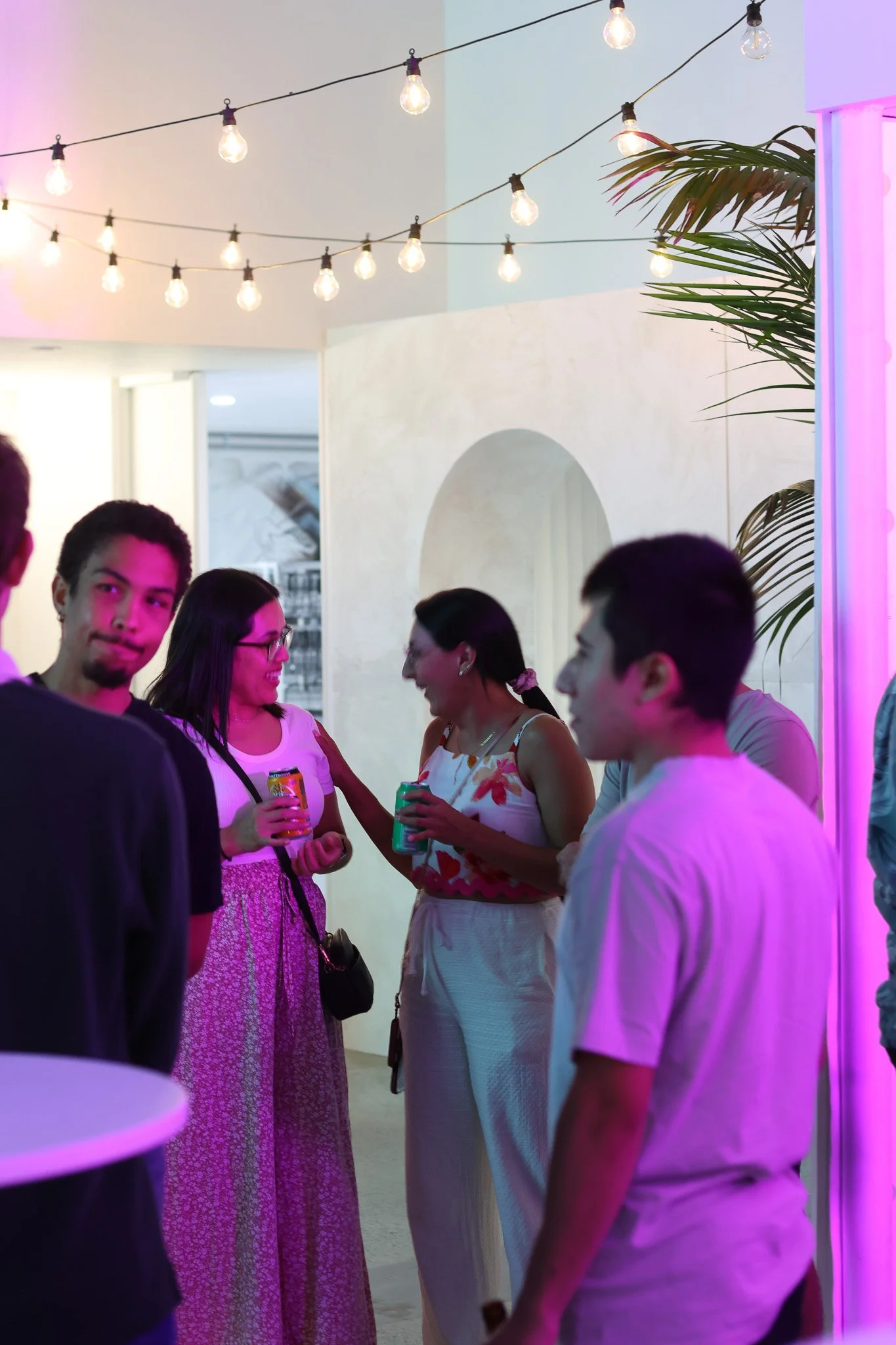 Group of people socializing at indoor party with colorful lighting and string lights.