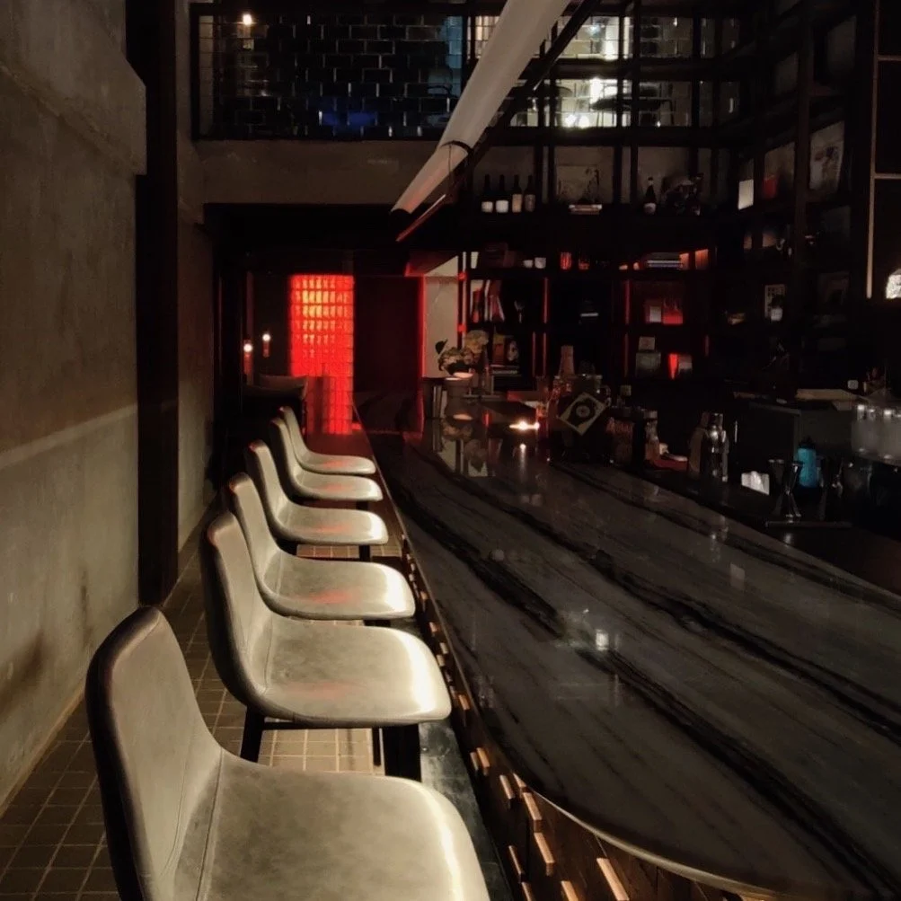 Dimly lit bar with a row of barstools along a dark marble bar counter