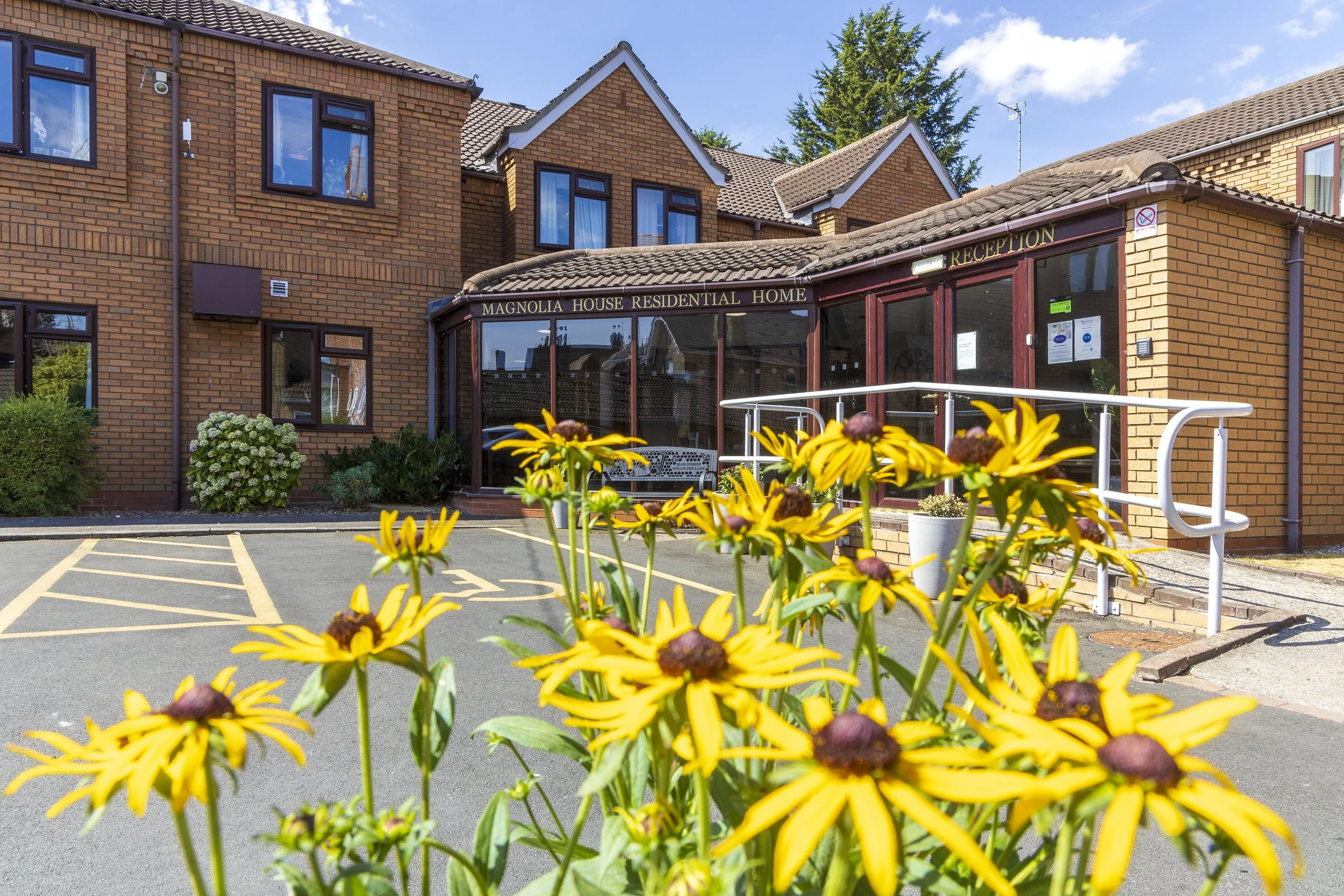 Magnolia House entrance with yellow flowers in the foreground and blue sky