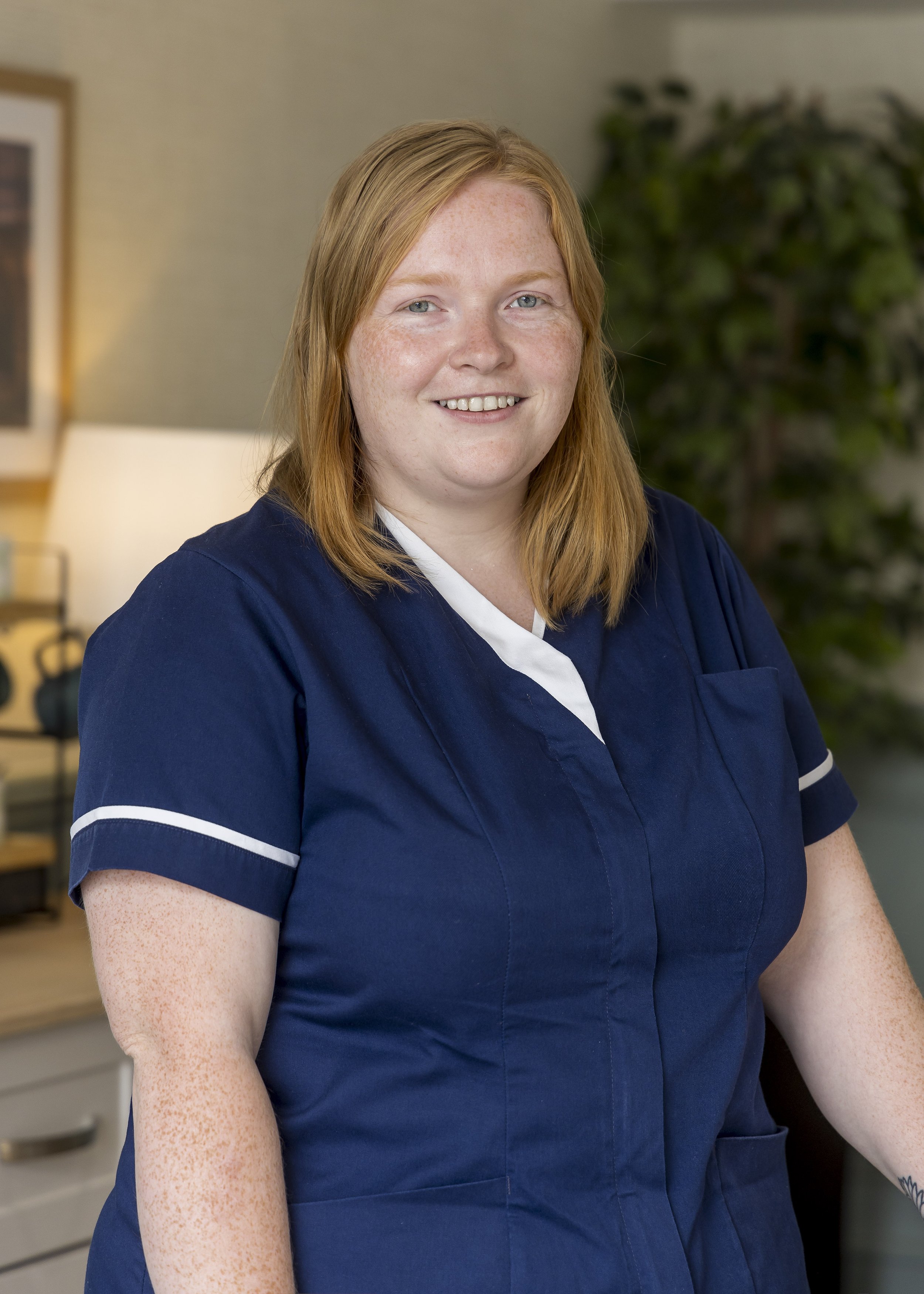 Smiling lady, shoulder length ginger hair, wearing a nurses uniform