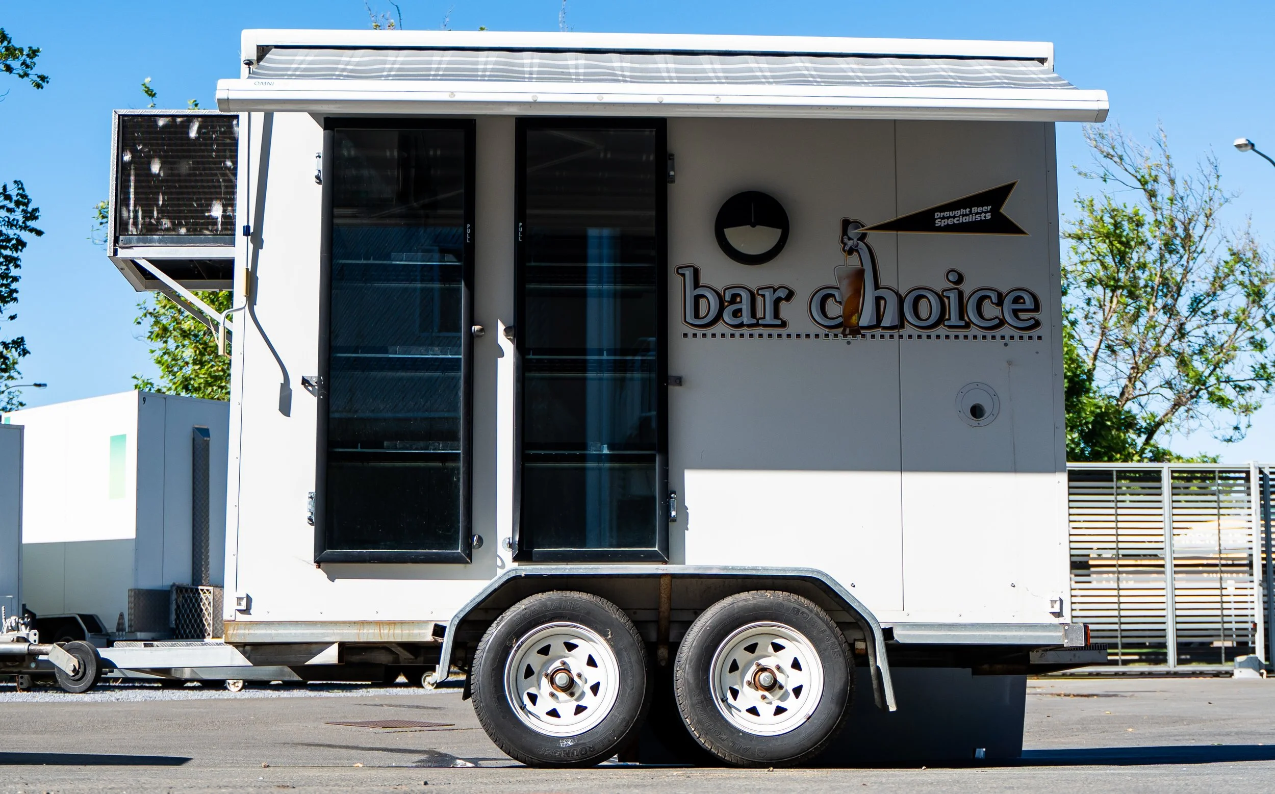 Mobile bar trailer with "bar choice" signage, parked outdoors on a sunny day.