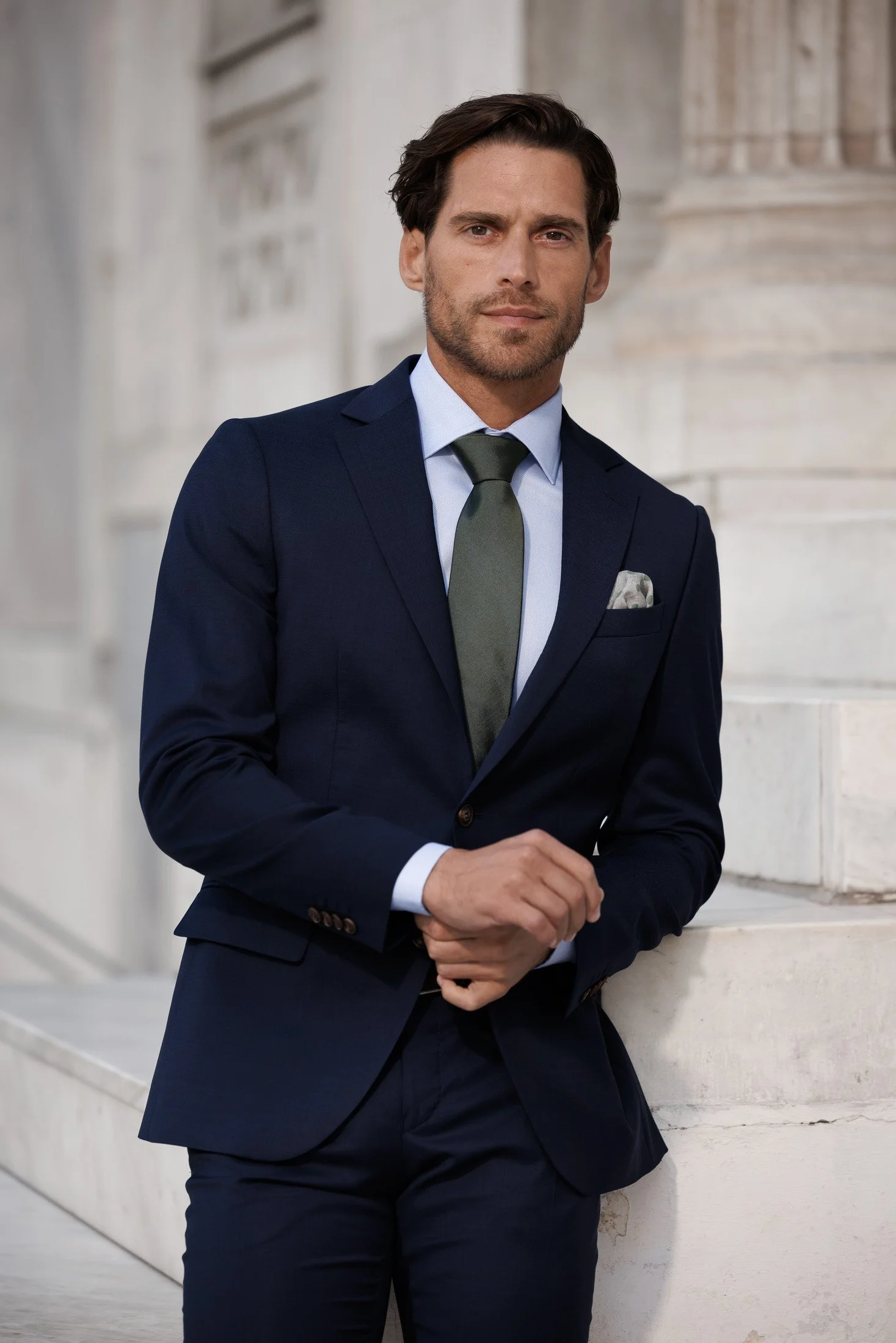 En mann i dress står ved en steinmur foran en klassisk bygning