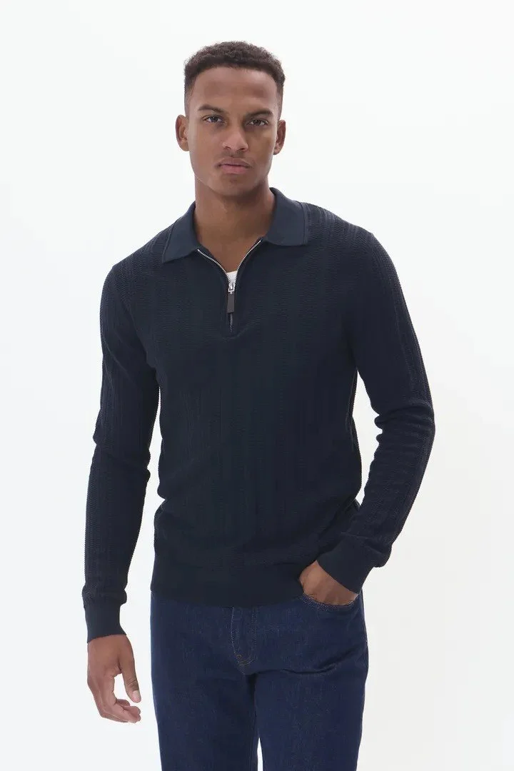 Ung mann i mørkeblå genser og jeans poserer mot en hvit bakgrunn.