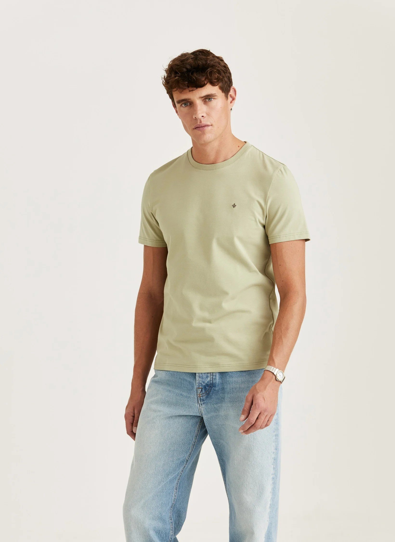 En ung mann i en lys grønn t-skjorte og lyse blå jeans står mot en hvit bakgrunn.