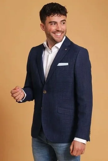 En mann i mørkeblå blazer og hvit skjorte som smiler, står mot en beige bakgrunn.