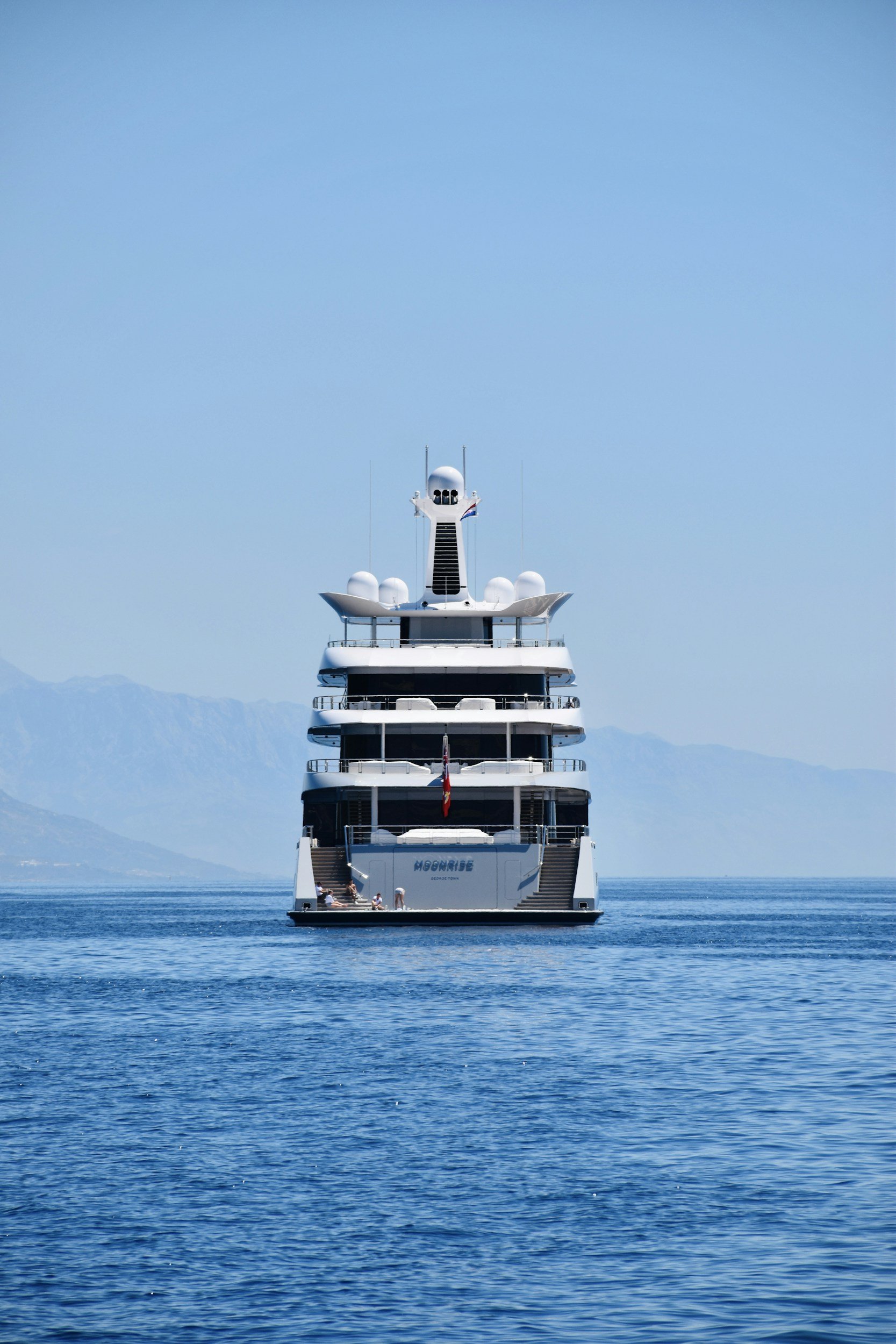 Large grey and white yacht cruising on calm blue water with mountains — representing luxury yacht ownership, deliveries, and captain services.