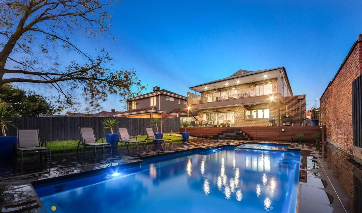 Backyard of a modern house with a swimming pool, outdoor seating, and landscaping at dusk.