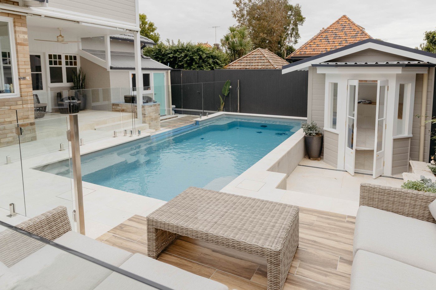 Modern house with glass walls, solar panels on the roof, a swimming pool, and lush green garden landscape.