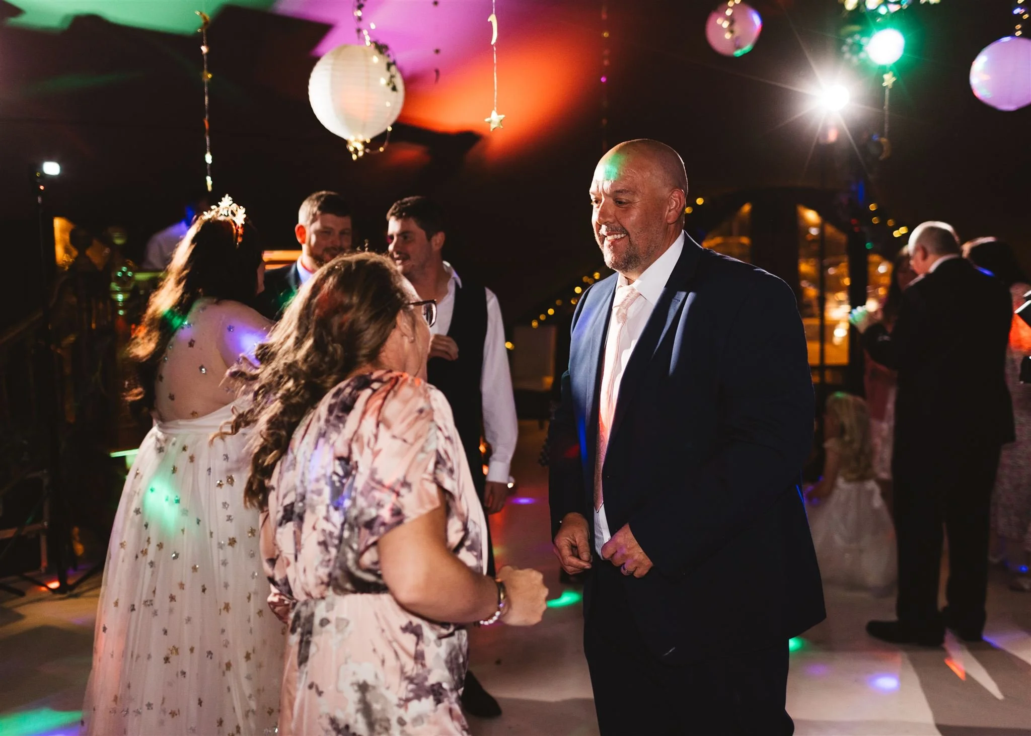 People dancing and socializing at a party with colorful lights and hanging decorations.