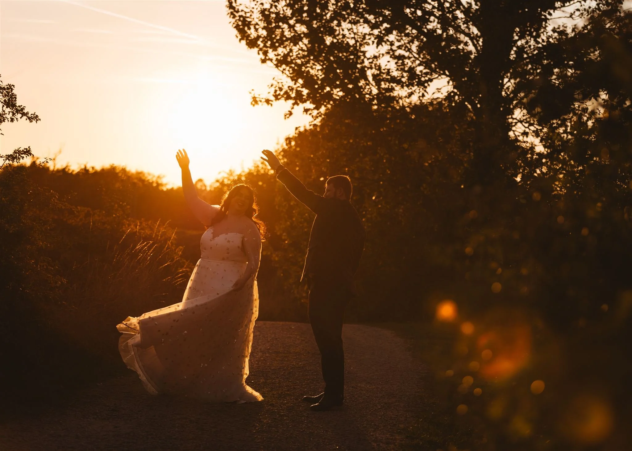 A couple dancing outdoors at sunset with silhouettes of trees in the background.