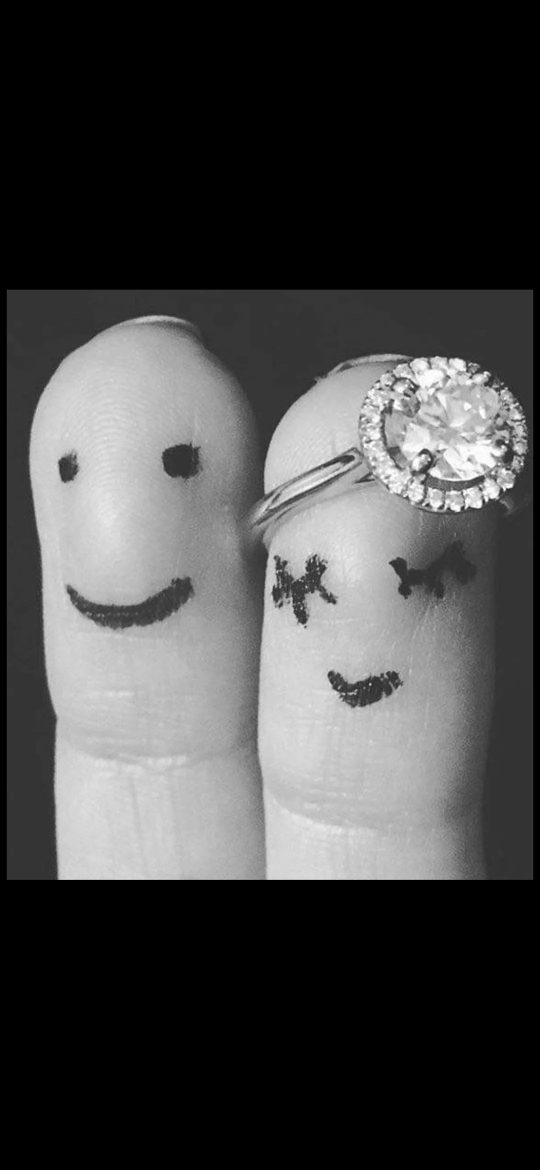 Two fingers with smiley face and kiss face drawings, one with a ring that has a large central diamond and smaller surrounding diamonds.