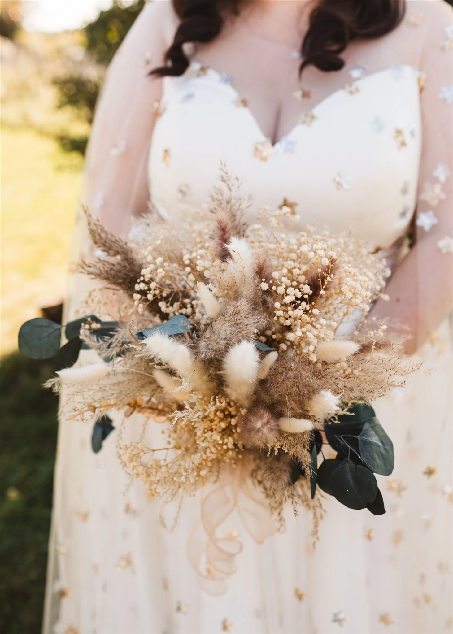 A woman in a white dress holding a bouquet of dried flowers.