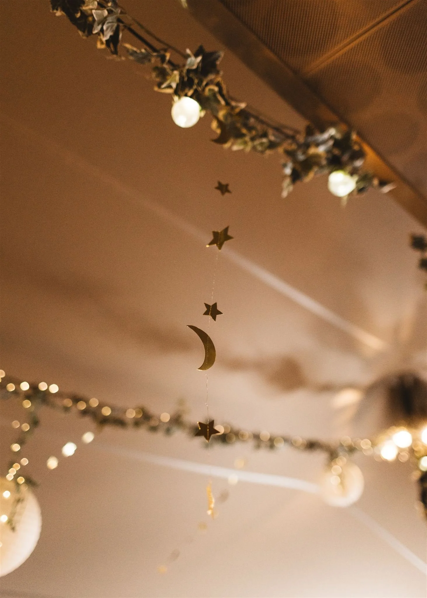 Decorative ceiling hanging with gold stars, a crescent moon, and fairy lights, with some festive tinsel in the corner.