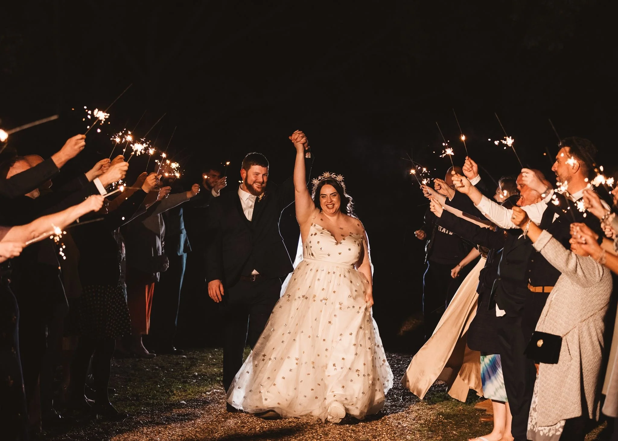 Bride and groom walking through a sparkler exit at night, surrounded by guests holding sparklers, celebrating their wedding.