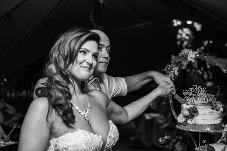 A bride and groom, possibly her father, cutting a wedding cake together at a celebration.