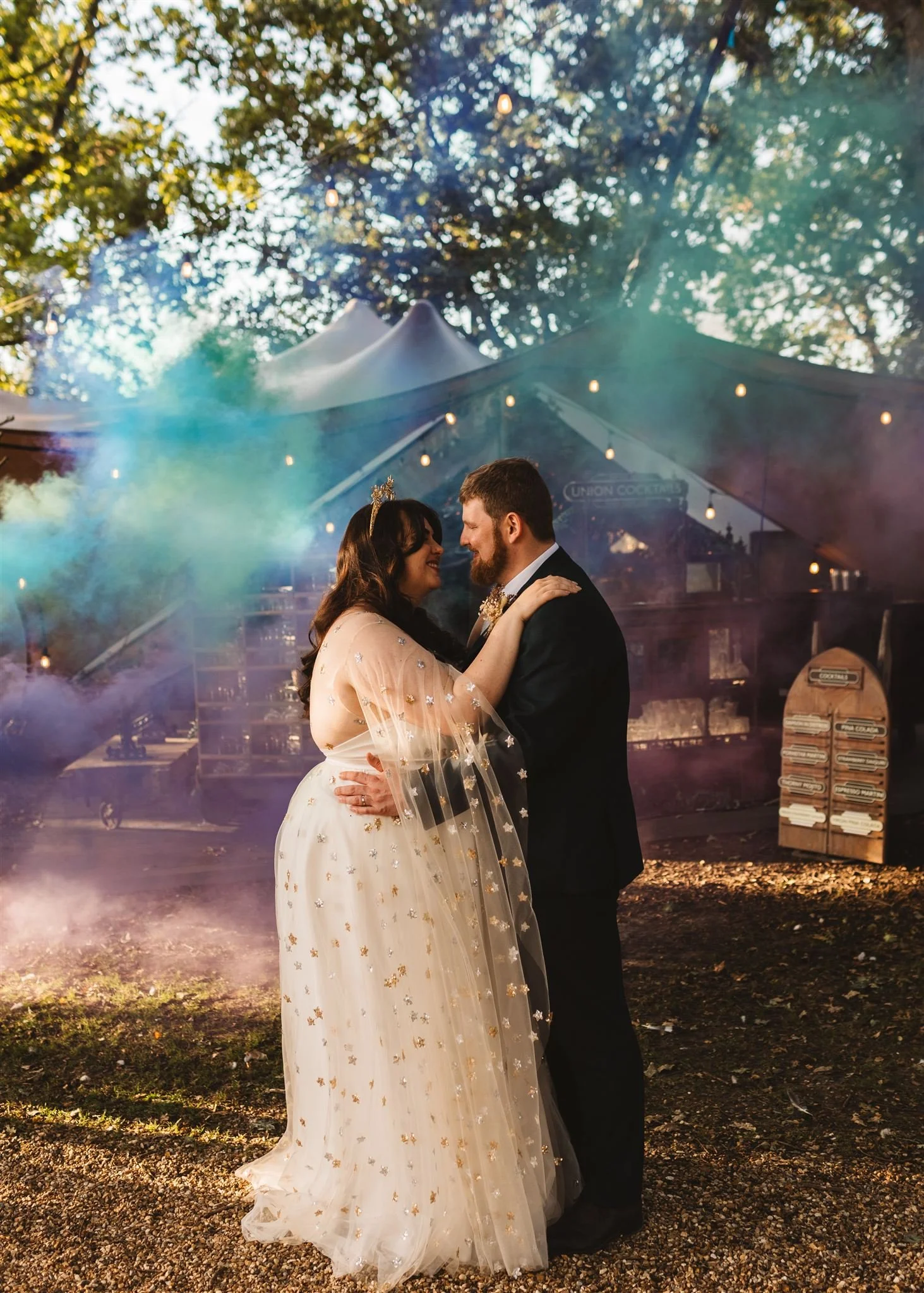 A newlywed couple dancing at their outdoor wedding reception with colorful lights and smoke effects in the background.