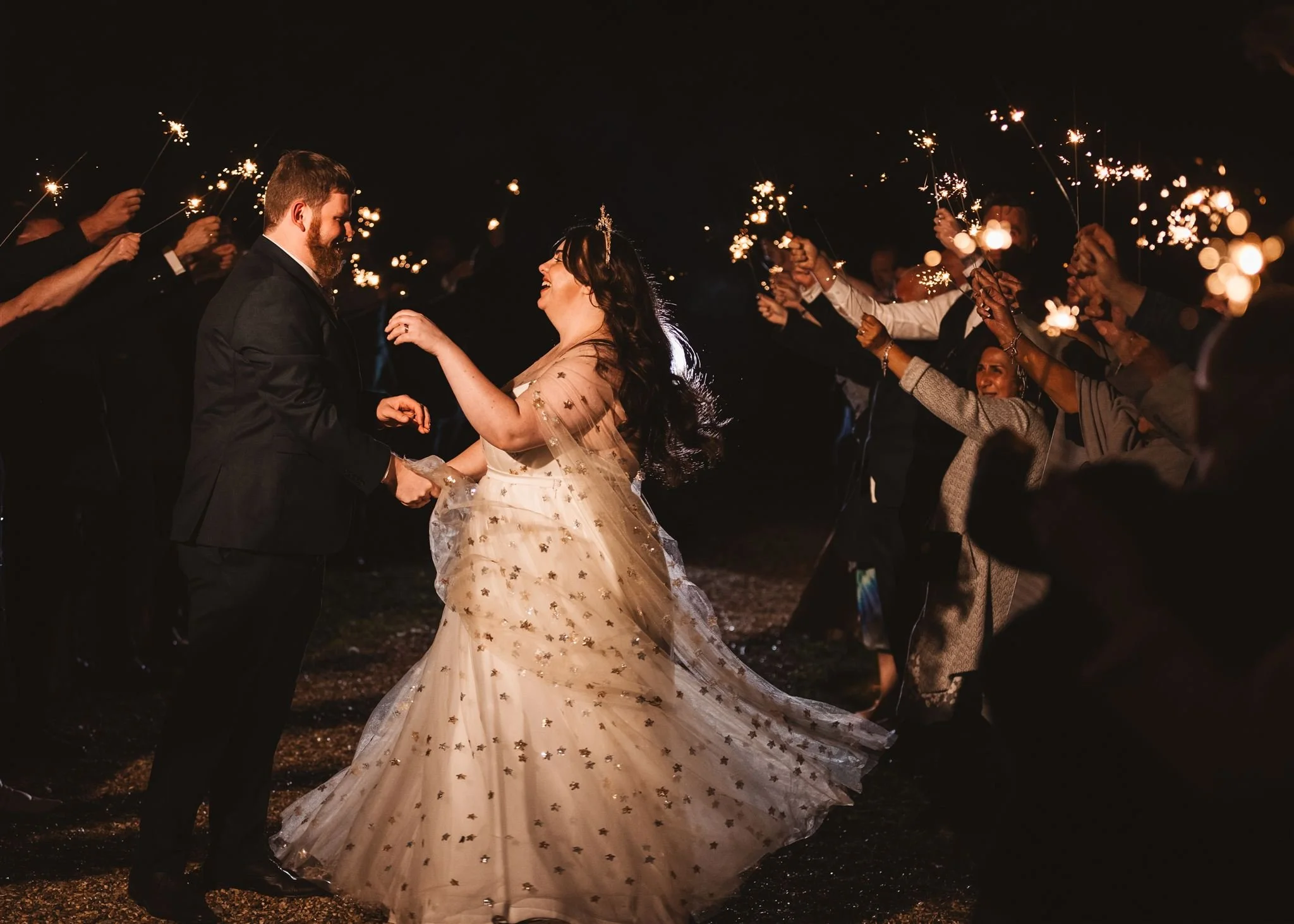 A bride and groom dancing at night surrounded by guests holding sparklers.