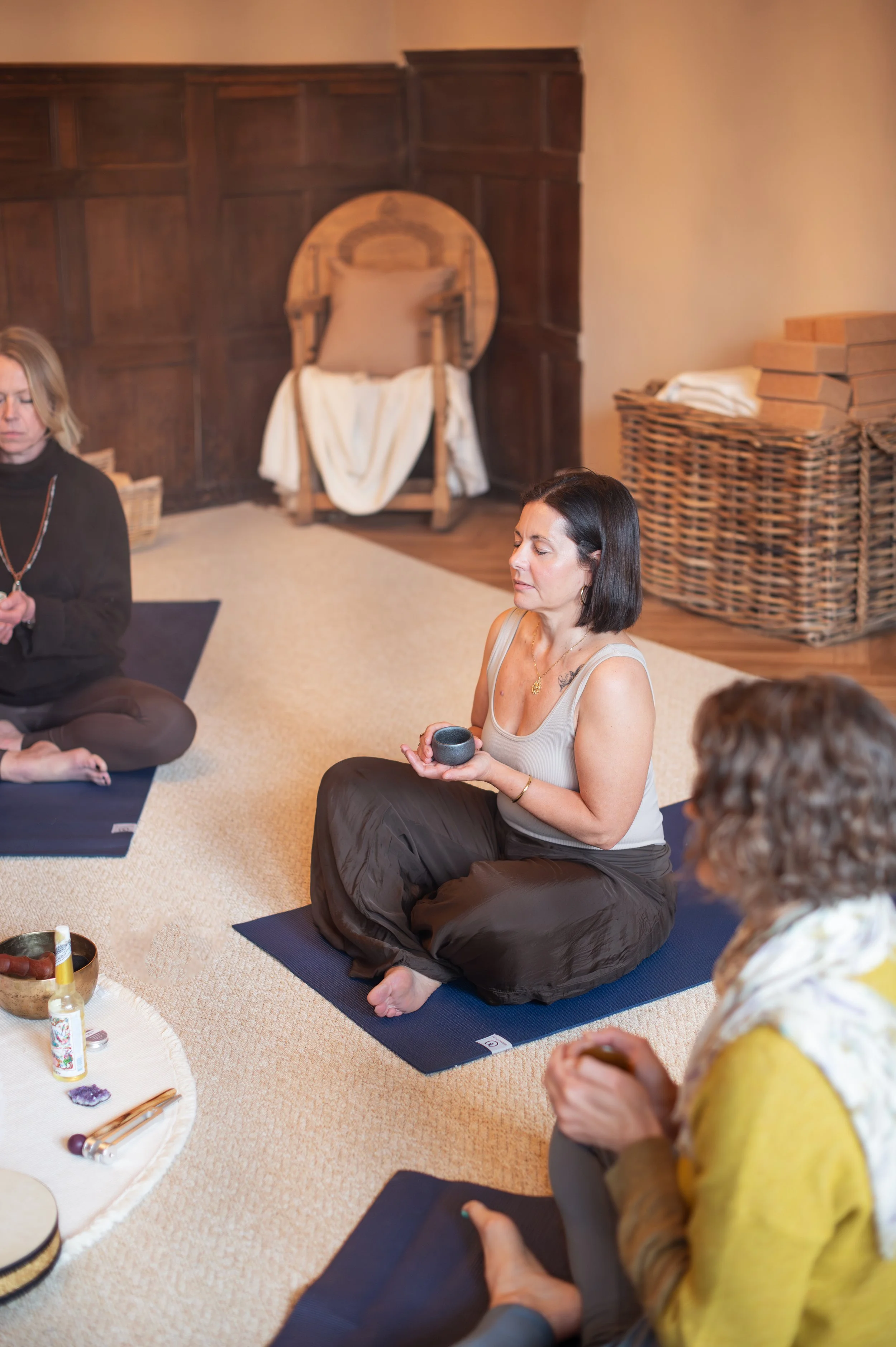 People participating in a meditation session in a cozy room with wooden walls, sitting on yoga mats, with a small table of crystals and a singing bowl nearby. Shot by Wellness Brand Photographer, Emily Dyer Creative
