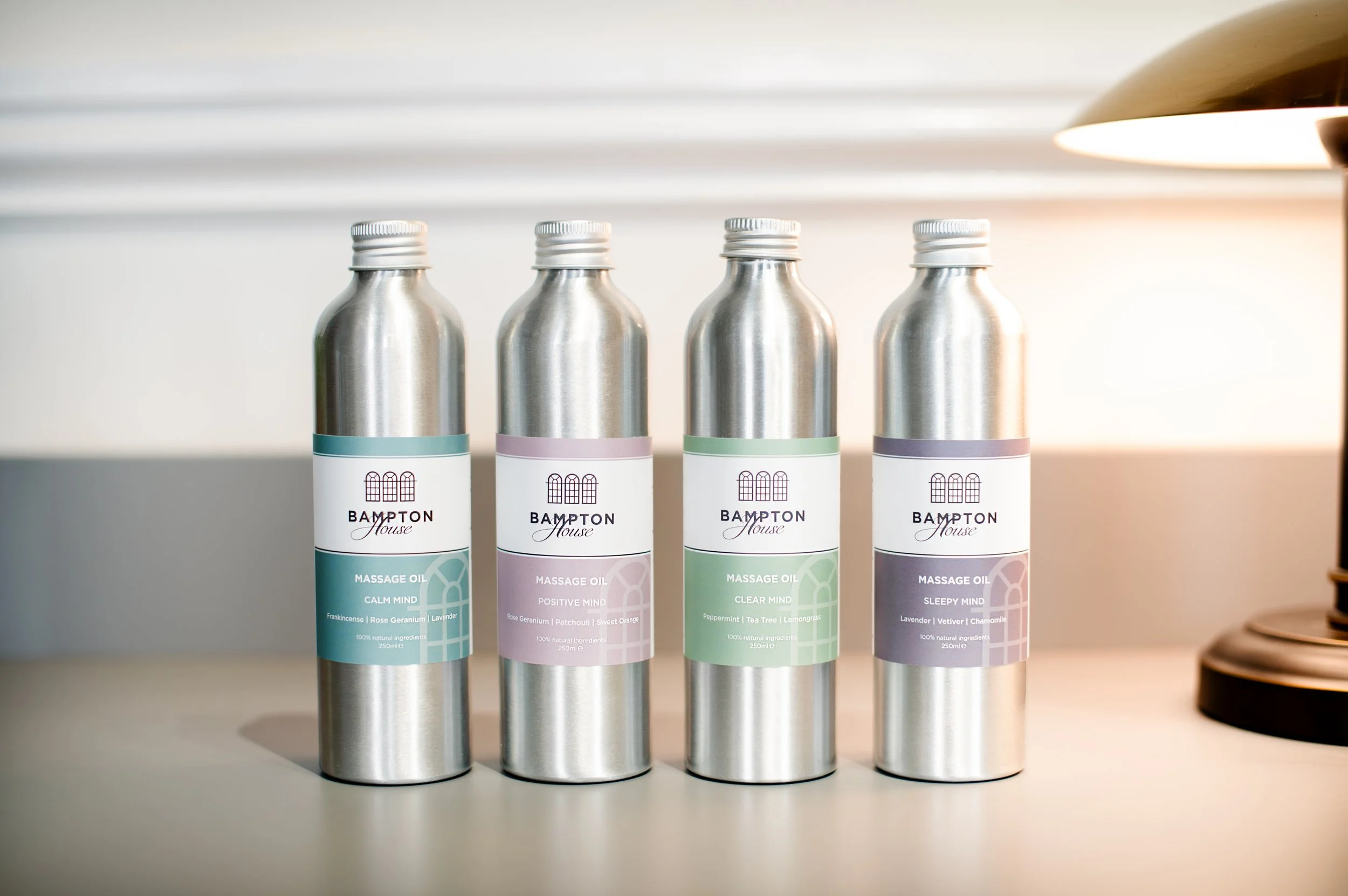 Four bottles of massage oil from Bampton House for wellness practitioners to use, each with different labels and scents, arranged in a row on a white surface. Shot in Witney, Oxfordshire, by Wellness Brand Photographer, Emily Dyer Creative