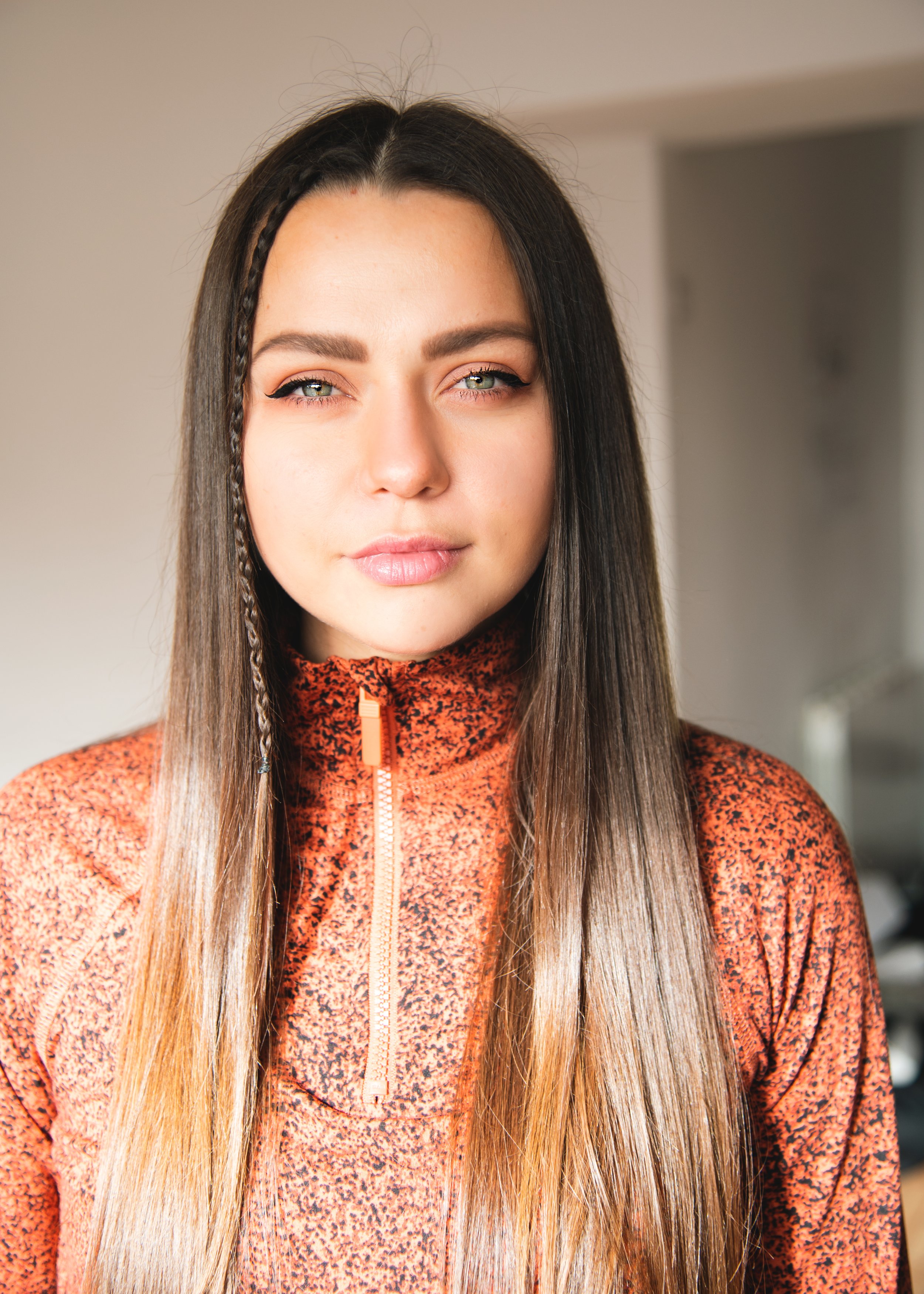 Close-up of a yoga teacher woman with long, straight hair, some of which is braided, wearing a patterned orange zip-up athletic top. Shot by Wellness Brand Photographer, Emily Dyer Creative
