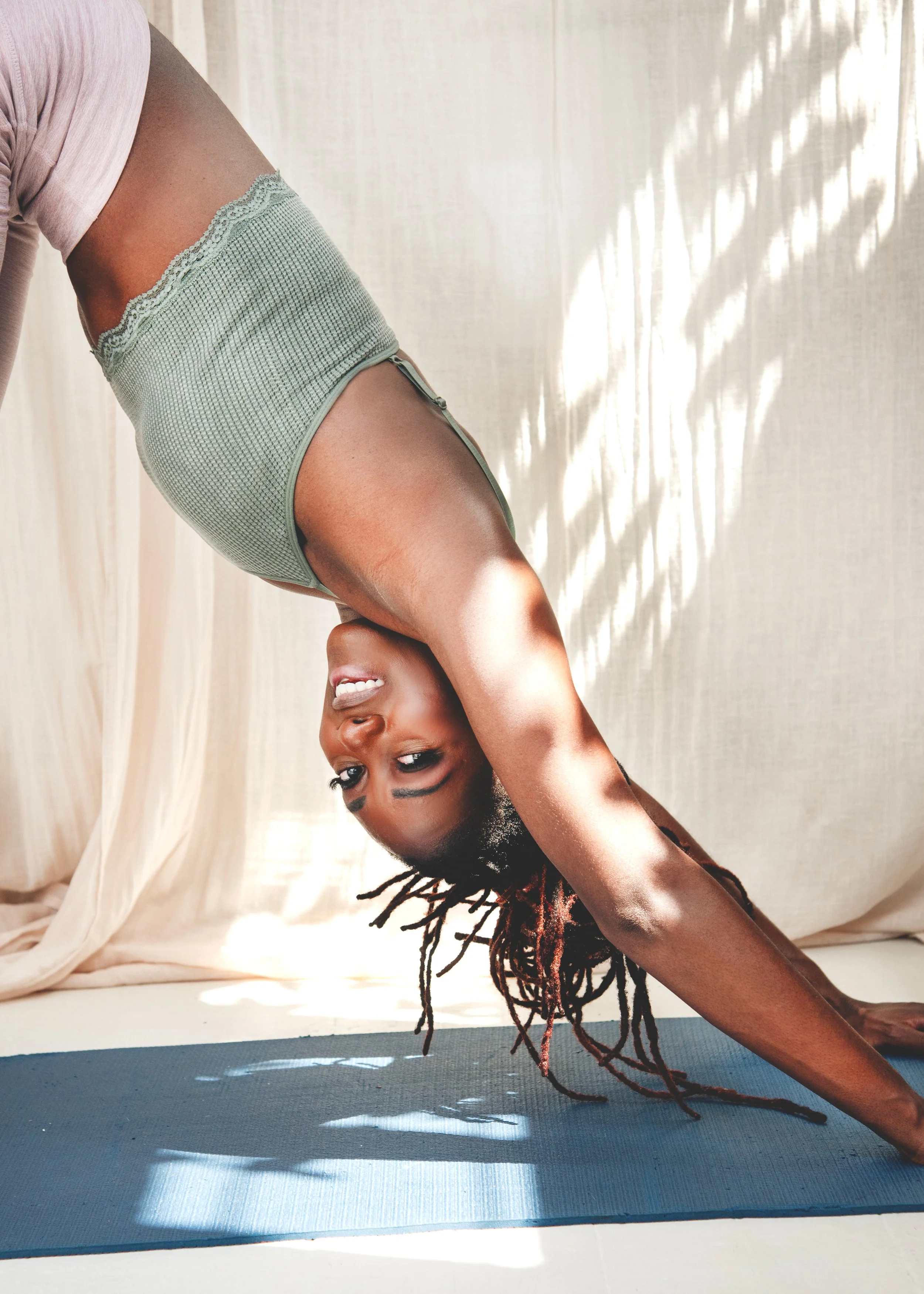 Woman performing a yoga pose on a blue mat indoors, with sheer curtains letting in natural light. Shot near Witney, Oxfordshire, by Wellness Brand Photographer, Emily Dyer Creative